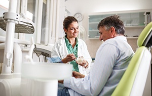 Smiling dentist showing patient model of teeth