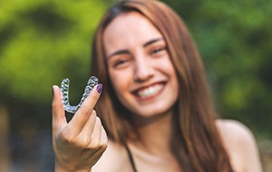 person smiling and holding up their Invisalign aligner