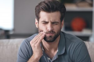 Pained man with hand on cheek from toothache at home