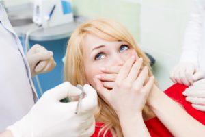 Scared woman with dental emergency covers mouth at dentist's office