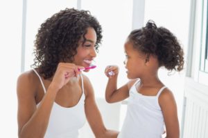 mother showing her daughter how to brush her teeth 