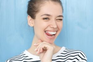 Woman standing in front of a light blue background wearing a striped shirt smiling